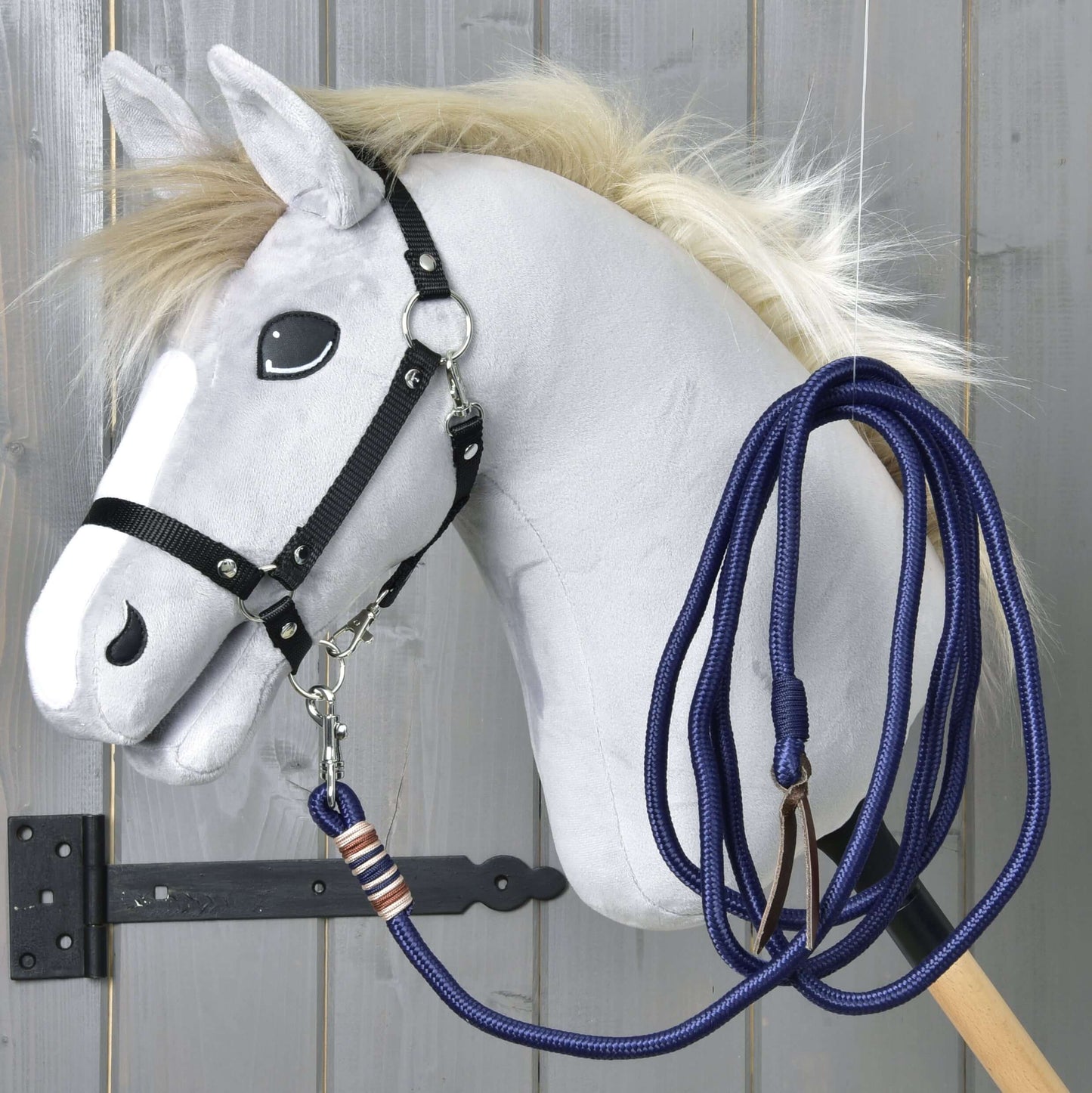 Hobby Horse - lonžovací vodítko od Hobby Horse LarDen s šedým koněm s huňatou hřívou, kreslenýma očima, černou uzdečkou a modrým vodítkem na dřevěné tyči, zobrazené před šedou dřevěnou stěnou.