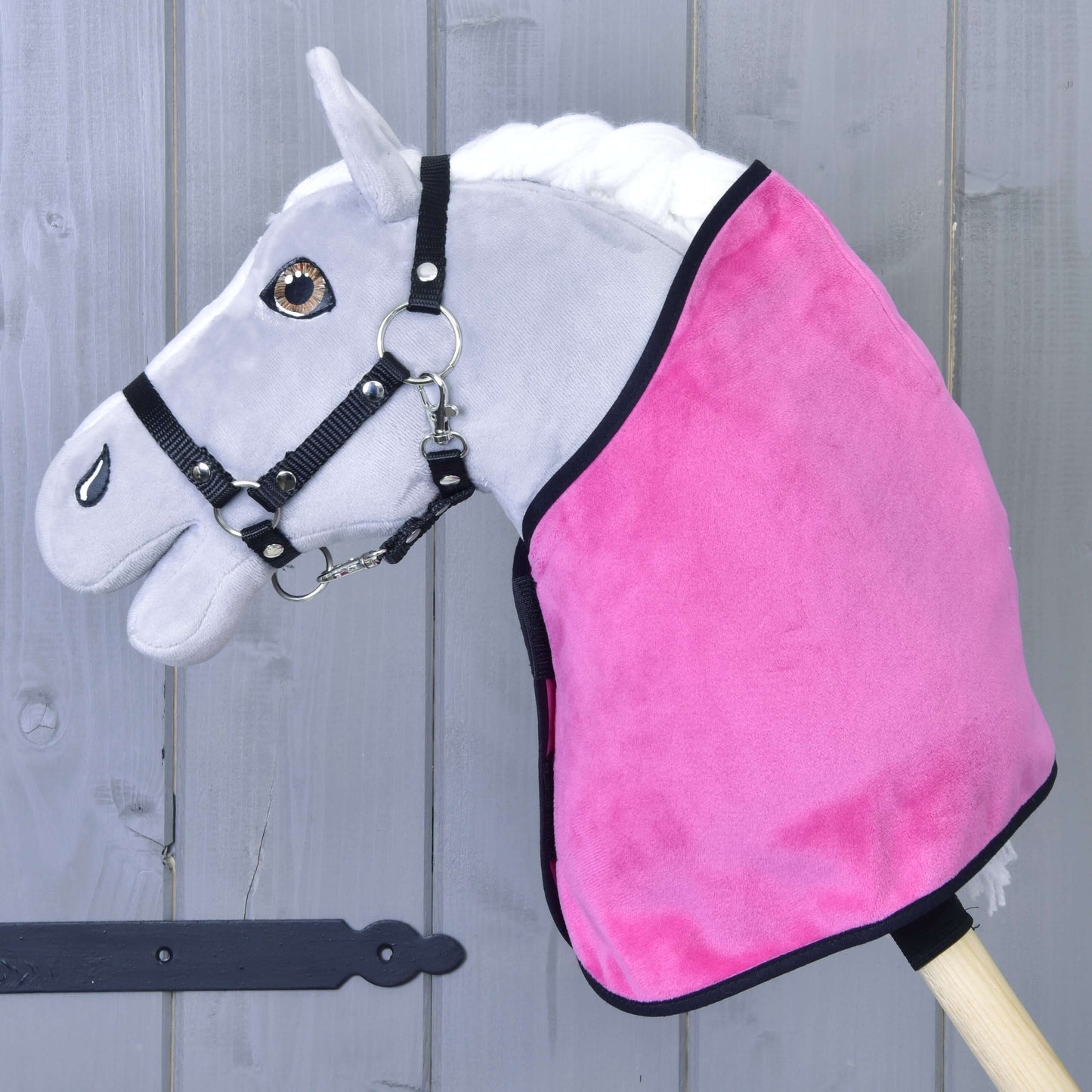 Set Hot Pink (čabraka + deka) od Hobby Horse LarDen se šedým Hobby Horse s černou uzdečkou, sytě růžovou dekou a ladící čabrakou na dřevěné tyči, zobrazený před rustikální šedou dřevěnou stěnou.