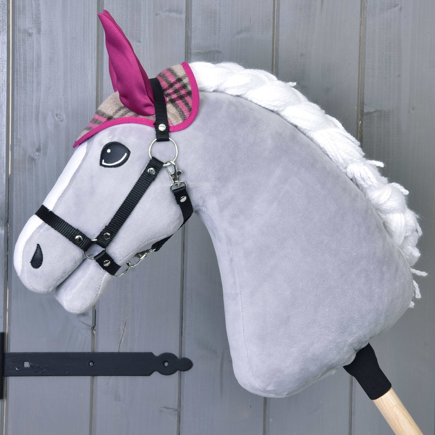 Šedý plyšový Hobby Horse od LarDen s bílou hřívou, růžovými a kostkovanými ušima a černou uzdečkou stojí na dřevěné tyči – perfektní v kombinaci se Set Cube Pink pro útulnou zábavu při hraní.