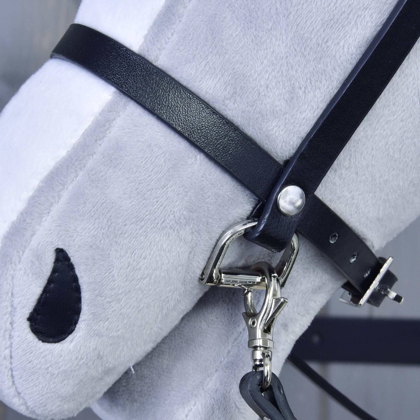 Detail hlavy světle šedého plyšového koně s černou uzdečkou z koženky od Hobby Horse LarDen, s kovovým kováním a jednoduchým černým vyšívaným okem.
