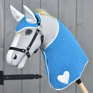Hobby Horse LarDen Set Mystery zobrazuje šedého koně s modrým texturovaným potahem připomínajícím deku, bílými ušima, bílým srdcem na boku, černou uzdečkou, hustou bílou hřívou, nasazeného na tyči před dřevěným pozadím.