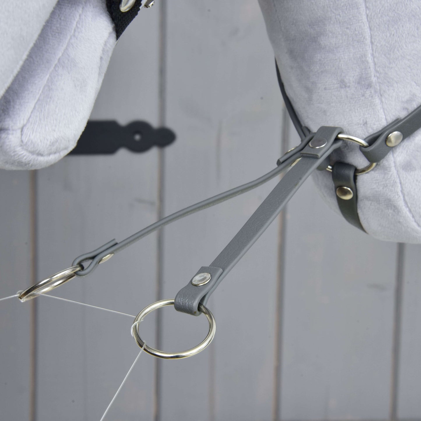 Martingale tmavě šedý od Hobby Horse LarDen, detail šedých kožených řemínků a koženkového martingalu s kovovými kroužky na světle šedé plyšové koňské hlavě na dřevěném pozadí.