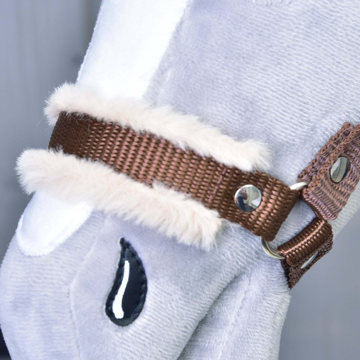 Detailní záběr na Ohlávku hnědou s beránkem od Hobby Horse LarDen, doplněk pro světle šedého plyšového Hobby Horse s hnědou ohlávkou, bílým lemem z umělé kožešiny, kovovými cvočky a prošitým černým detailem ve tvaru kapky.