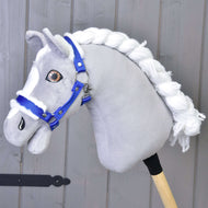 Šedý látkový Hobby Horse s bílou přízovou hřívou a ohlávkou Hobby Horse LarDen Ohlávka modrá s beránkem stojí před světle šedou dřevěnou stěnou.