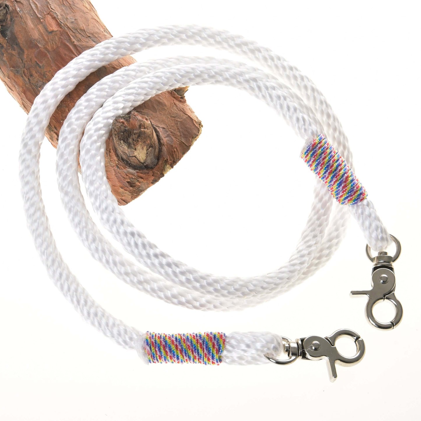 Otěže bílé od Hobby Horse LarDen s kovovými karabinami na obou koncích a duhově barevnou nití u každé karabiny, stočené na dřevě na bílém pozadí, připomínající kvalitní otěže k bezudidlové uzdečce.