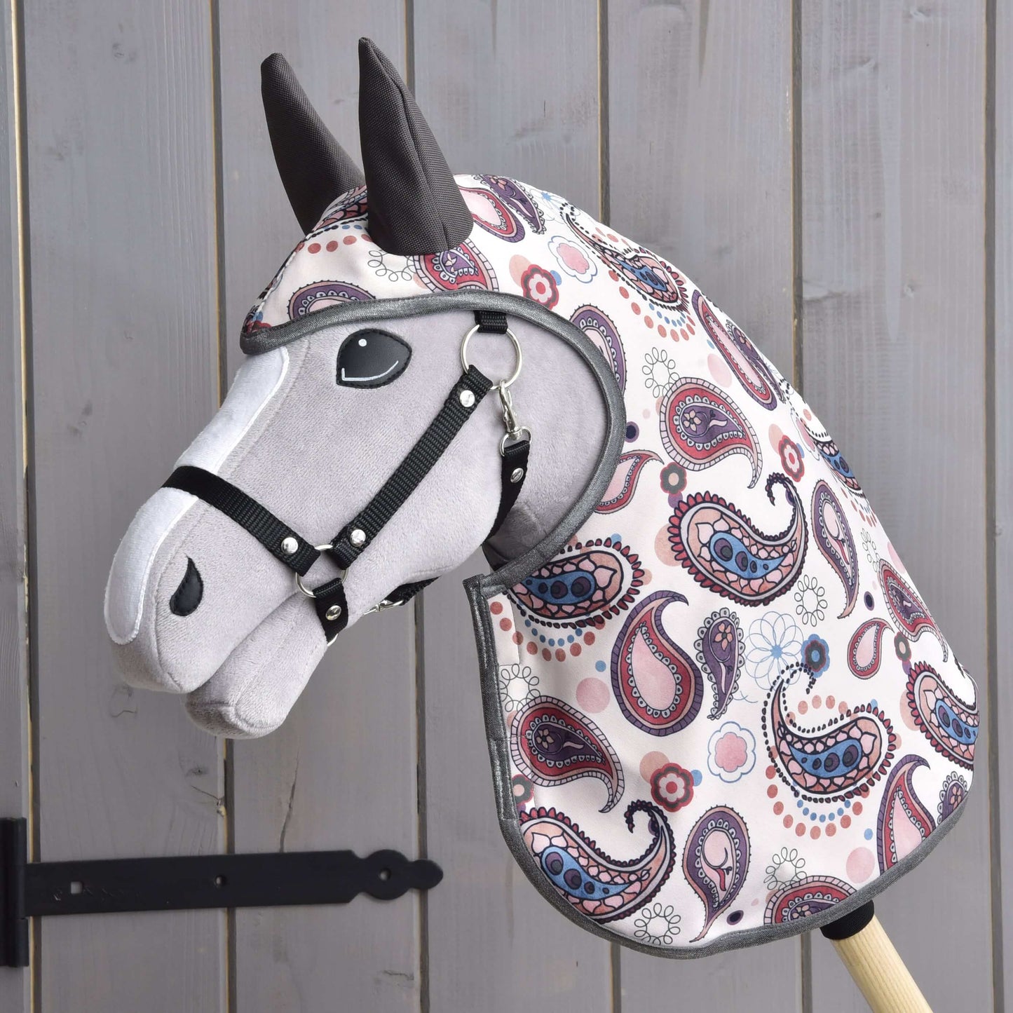 Pláštěnka Fairy Blue (softshell) od Hobby Horse LarDen na látkovém Hobby Horse se šedou hlavou, černou uzdečkou a barevným kašmírovým potahem, před dřevěným obložením.