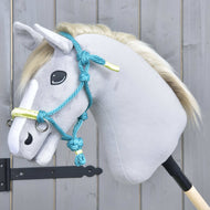 Hobby Horse LarDen Parelka Tyrkys na plyšovém Hobby Horse se světle šedou hlavou, bílou hřívou a modrou uzdečkou, nasazeném na dřevěné tyči před šedou dřevěnou stěnou.