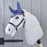 Čabraka háčkovaná Blue sport od Hobby Horse LarDen je zobrazena na plyšovém Hobby Horse s bílým obličejem a černou uzdečkou, nasazeném na dřevěné tyči před šedými panelovými dveřmi s černým pantem.