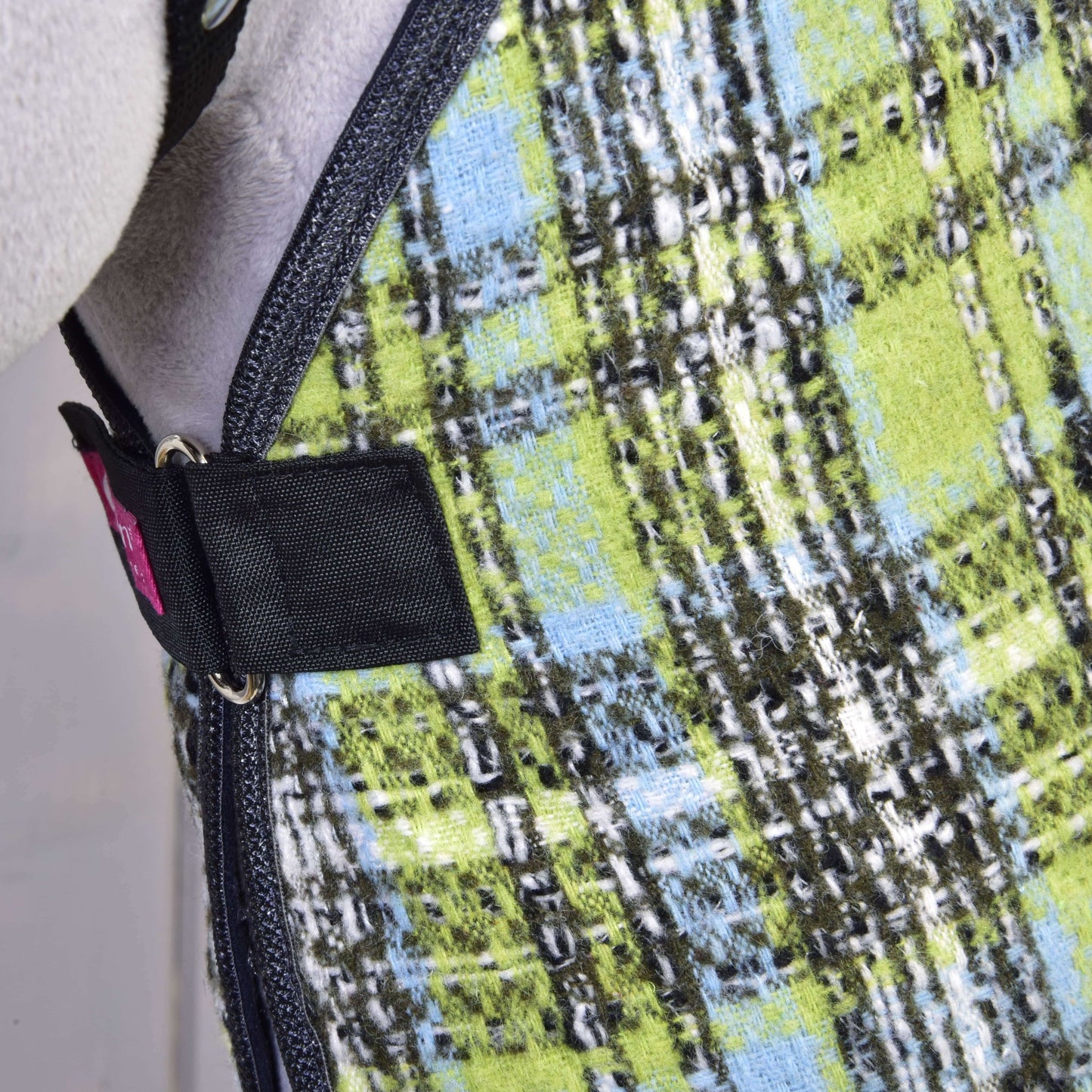 Detail deky Deka stájová Lemon Blue od Hobby Horse LarDen, zobrazující zelenou, modrou, černou a bílou kostkovanou látku s černým popruhem a kovovou přezkou – ideální pro ochranu koně nebo trénink.