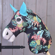 Hobby Horse ochranný oblek Pineapple (Lycra) od Hobby Horse LarDen má černou hlavu s výrazným potiskem ananasů a listů, modré uši a bílý čenich, je nasazený na dřevěné tyči a zobrazený před šedou dřevěnou stěnou.