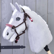 Hobby Horse LarDen Parelka York na šedé plyšové hlavě Hobby Horse s bílou hřívou a bílou skvrnou na nose, s hnědou pletenou provazovou ohlávkou, zavěšené na šedé dřevěné stěně.