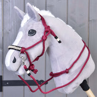 Hobby Horse LarDen Provazový set Burgundy na šedém plyšovém Hobby Horse s bílou hřívou, černým nosem a vínovou provazovou ohlávkou, na dřevěné tyči před šedou dřevěnou stěnou.