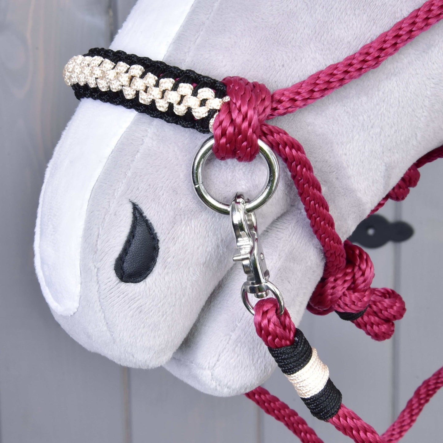 Detail hlavy Hobby Horse LarDen s Provazovým setem Burgundy, s červenou a černou provazovou ohlávkou se stříbrnou karabinou, pleteným páskem, jednoduchým vyšitým černým okem, měkkým šedým nosem a ladícími otěžemi.