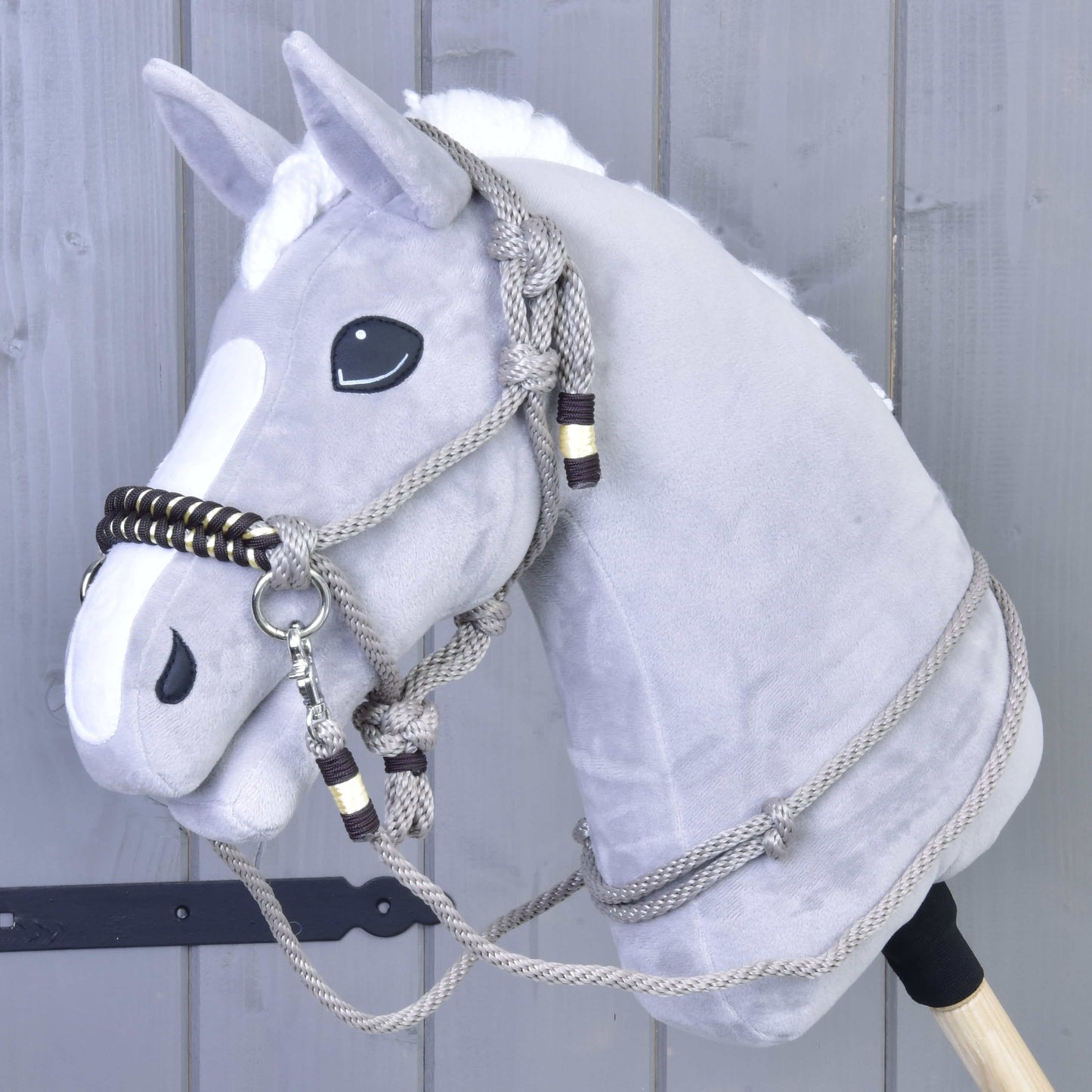 Provazový set Splendid od Hobby Horse LarDen na šedém plyšovém Hobby Horse s bílou hřívou, černýma očima a provazovou uzdečkou s otěžemi, před šedou dřevěnou stěnou.