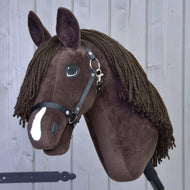 Hobby Horse Chianti s černou ohlávkou od Hobby Horse LarDen, hnědý plyšový Hobby Horse s černou ohlávkou, knoflíkovýma očima, přízovou hřívou a bílou skvrnou na nose inspirovaný American Quarter Horse, pózuje před světle šedým dřevěným pozadím.