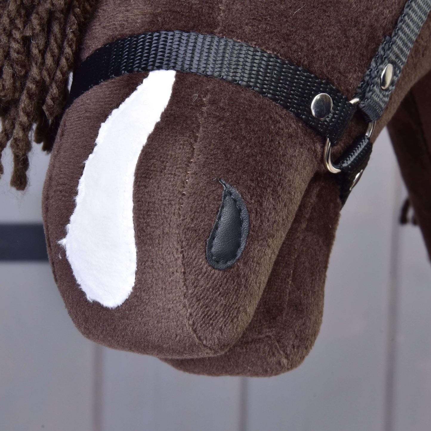 Detail Hobby Horse Chianti s černou ohlávkou od Hobby Horse LarDen: hnědá látková hlava koně s bílou skvrnou, černou ohlávkou, knoflíkovým okem a hnědou přízovou hřívou na jemně pruhovaném světlém pozadí.