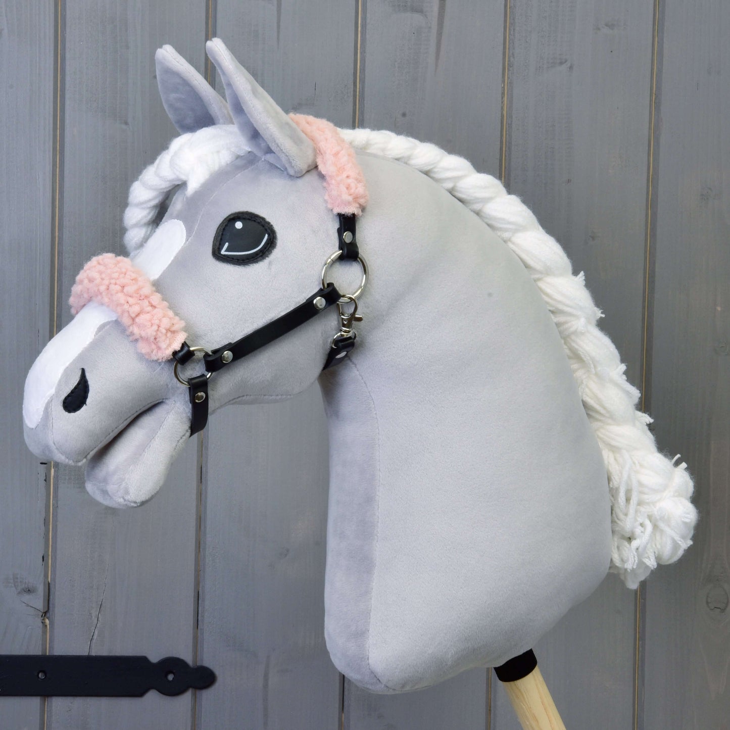 Plyšový Hobby Horse LarDen s šedým obličejem, bílou hřívou a černou ohlávkou se starorůžovým beránkem z koženky na dřevěném pozadí.