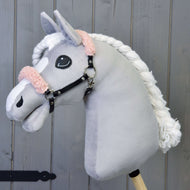 Plyšový Hobby Horse LarDen s šedým obličejem, bílou hřívou a černou ohlávkou se starorůžovým beránkem z koženky na dřevěném pozadí.