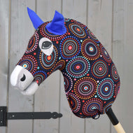 Hobby Horse ochranný oblek Alice od Hobby Horse LarDen s barevnou vzorovanou hlavou, modrýma plstěnýma ušima a výraznýma očima na dřevěné tyči, zobrazený před světle šedou dřevěnou stěnou.