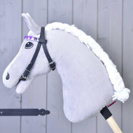 Uzdečka bez nánosníku fialová se 2 čelenkami (vel. M) od Hobby Horse LarDen, se šedým plyšovým koněm s bílou pletenou hřívou, černou uzdečkou bez nánosníku a fialovou stuhou s kosočtvercovým vzorem na dřevěné tyči, u světle šedé dřevěné stěny.