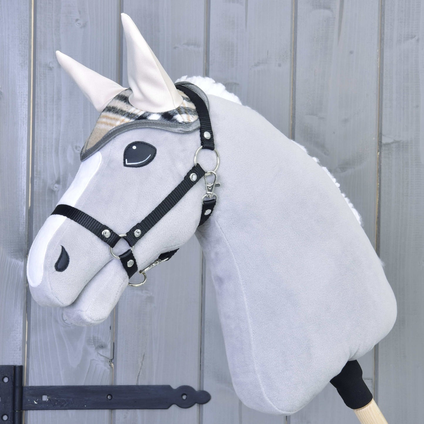 Plyšový šedý Hobby Horse od Hobby Horse LarDen má na sobě čabraku Cremo England a černou ohlávku, je nasazený na dřevěné tyči před světle šedým dřevěným plotem.