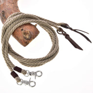 Westernové otěže Dallas rozdělené od Hobby Horse LarDen, béžové stočené pletené lano s koženými detaily a dvěma kovovými karabinami na koncích, zobrazené přehozené přes dřevo na bílém pozadí.