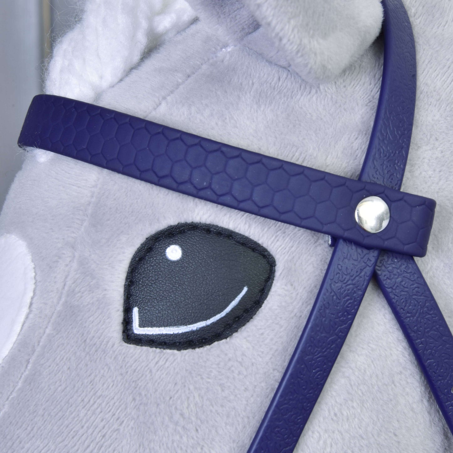 Detail obličeje plyšového koně s vyšitým černo-bílým okem, s Kompletní uzdečka s nánosníkem Dark Purple od Hobby Horse LarDen; uzdečka má stříbrný knoflíkový detail a srst koně je světle šedá.