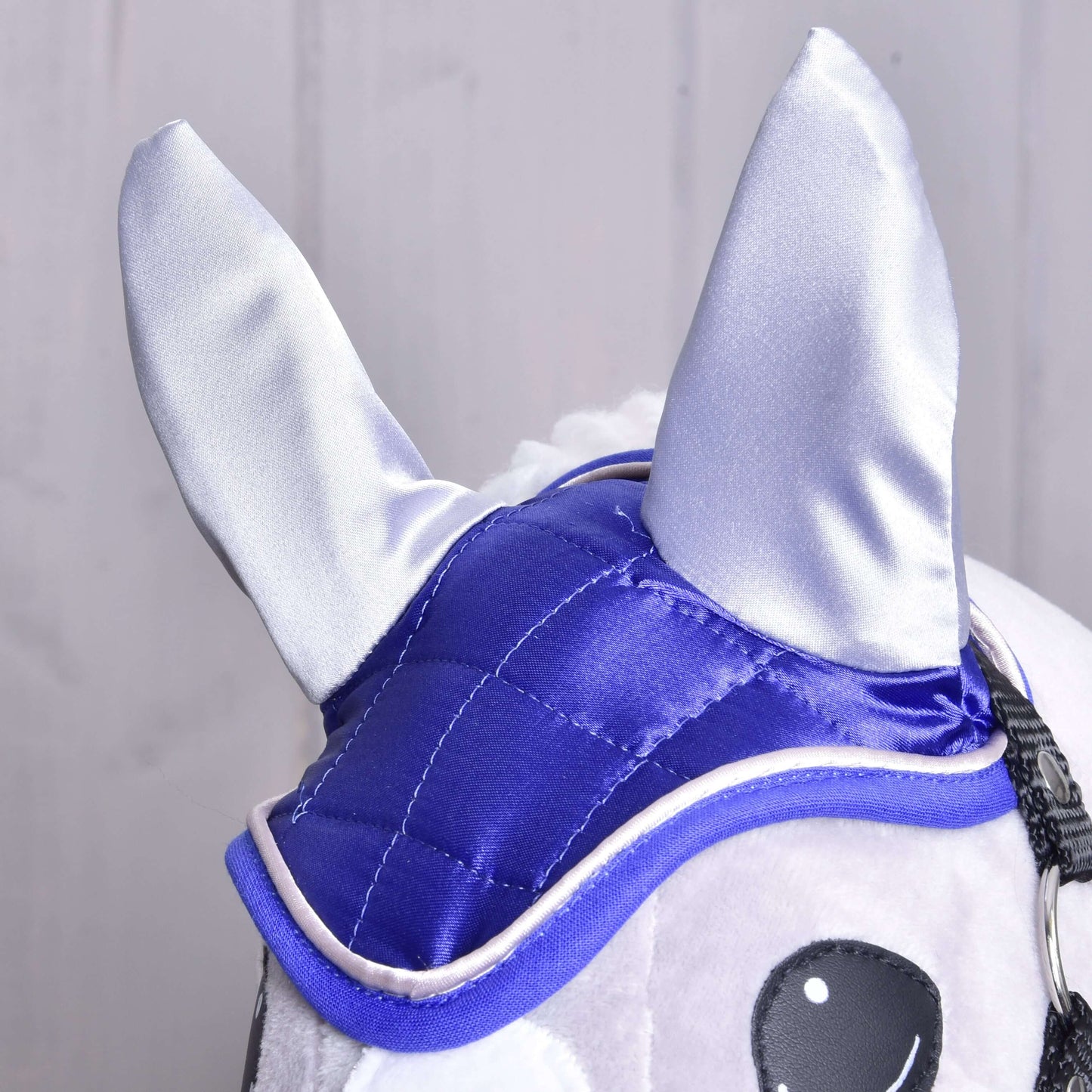 Detail čabraky DeLuxe Blue od Hobby Horse LarDen na plyšovém Hobby Horse, s lesklou modrou a stříbrnou látkou pro ochranu proti hmyzu, velkými špičatými ušmi a černobíle vyšívanýma očima na světlém pozadí.