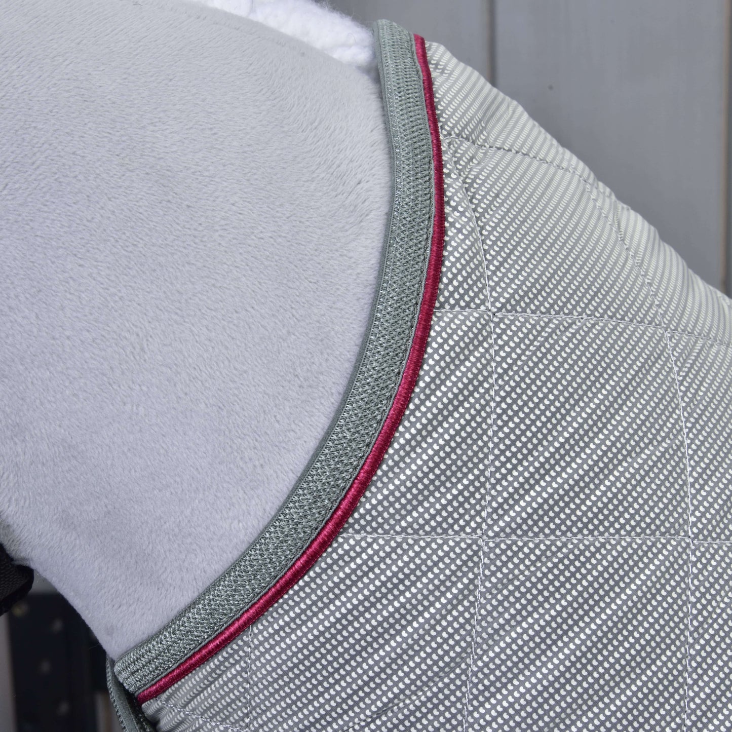 Detail Hobby Horse LarDen Deka Silver Eleganza, světle šedé prošívané tréninkové deky s mřížkovým vzorem, šedým lemováním a tmavě růžovou paspulkou, přehozené přes měkký bílý povrch.