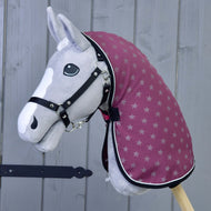 Šedý Hobby Horse od Hobby Horse LarDen s černou uzdečkou, vínovou kapucí se vzorem hvězd a dekou Deka stájová Purple stojí před šedým dřevěným pozadím. Má bílou lysinu a černé knoflíkové oči.