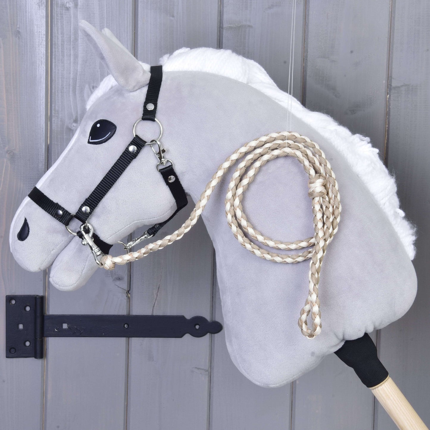 Hobby Horse - pletené vodítko Double Latte od Hobby Horse LarDen, šedý Hobby Horse s černou uzdečkou a pletenými otěžemi, zobrazený před šedou dřevěnou stěnou.
