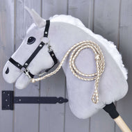 Hobby Horse - pletené vodítko Double Latte od Hobby Horse LarDen, šedý Hobby Horse s černou uzdečkou a pletenými otěžemi, zobrazený před šedou dřevěnou stěnou.