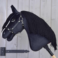 Hobby Horse Freya s černou ohlávkou od Hobby Horse LarDen s bílým pruhem na obličeji a černou přízovou hřívou na dřevěné tyči je umístěná před světle šedou dřevěnou stěnou – ideální pro každého rodinného nadšence do koní.