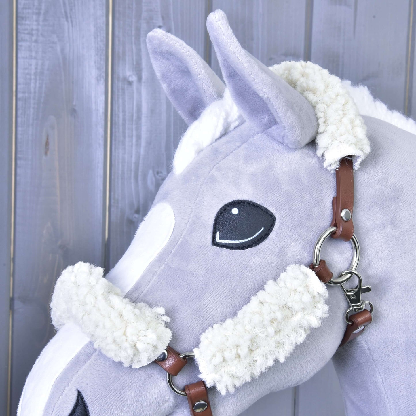 Detail hračky Hobby Horse LarDen s hnědou ohlávkou z koženky s kompletním beránkem, šedými fleecovými detaily a dřevěným pozadím.