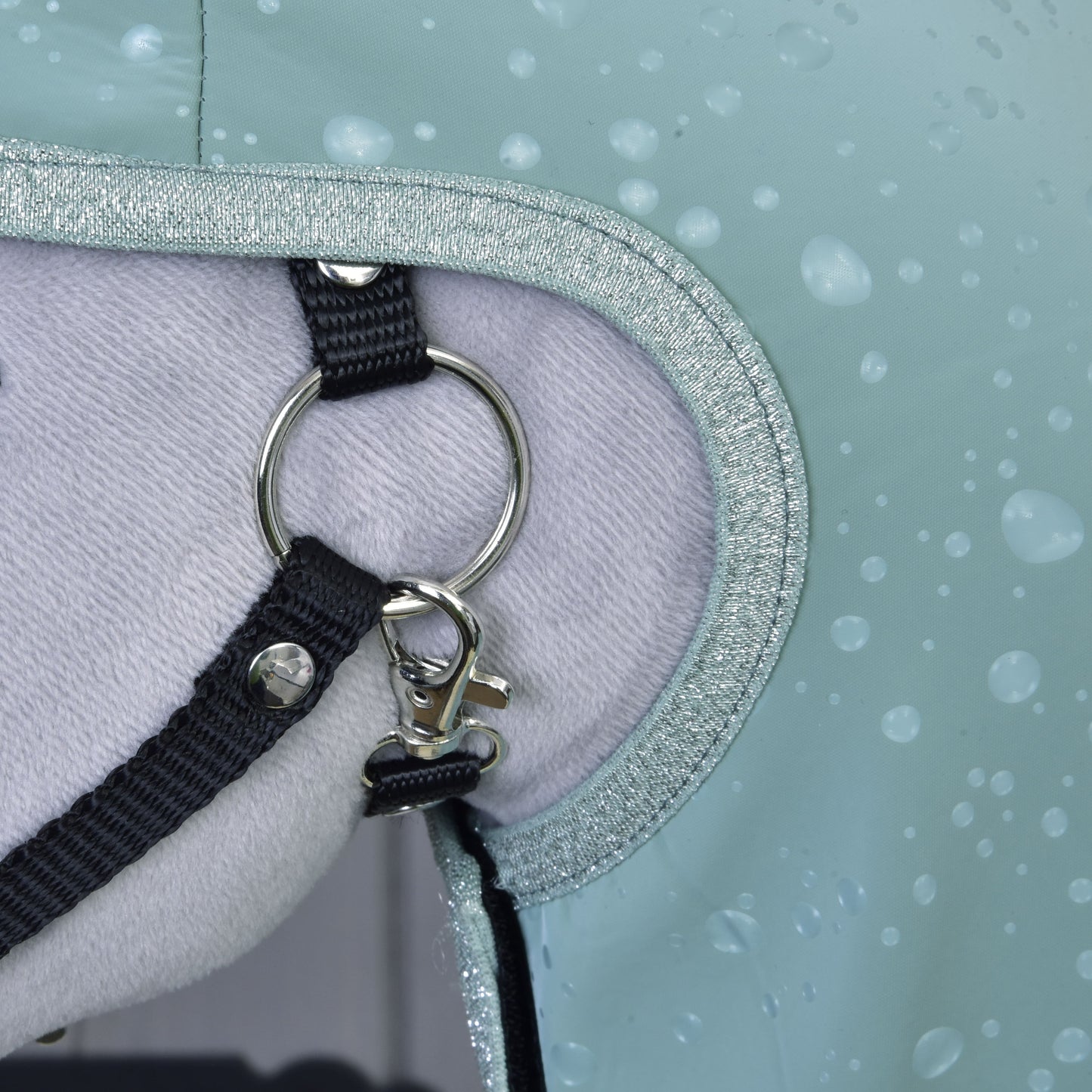 Detail koně s pláštěnkou Hobby Horse LarDen Raincoat Greeny, s kovovým kroužkem, černým popruhem, klipem a měkkou světlou podšívkou s kapkami — poskytuje ochranu za každého počasí.
