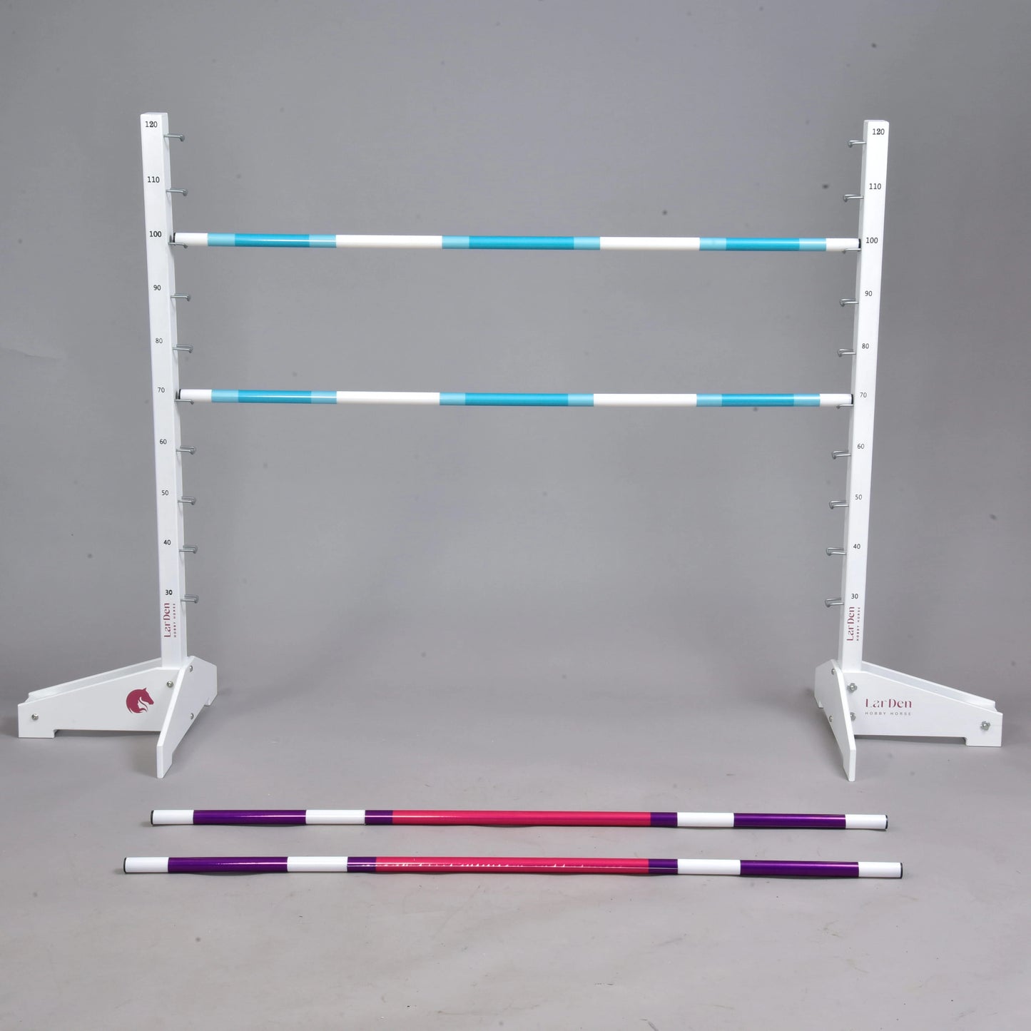 Set překážky kolmák 120 cm + 2 ks bariérky od Hobby Horse LarDen s bílým nastavitelným stojanem nesoucím dvě modrobílé pruhované tyče a červené a fialové bariérky na šedé podlaze. Ideální pro Hobby Horsing, s jednolitým šedým pozadím.