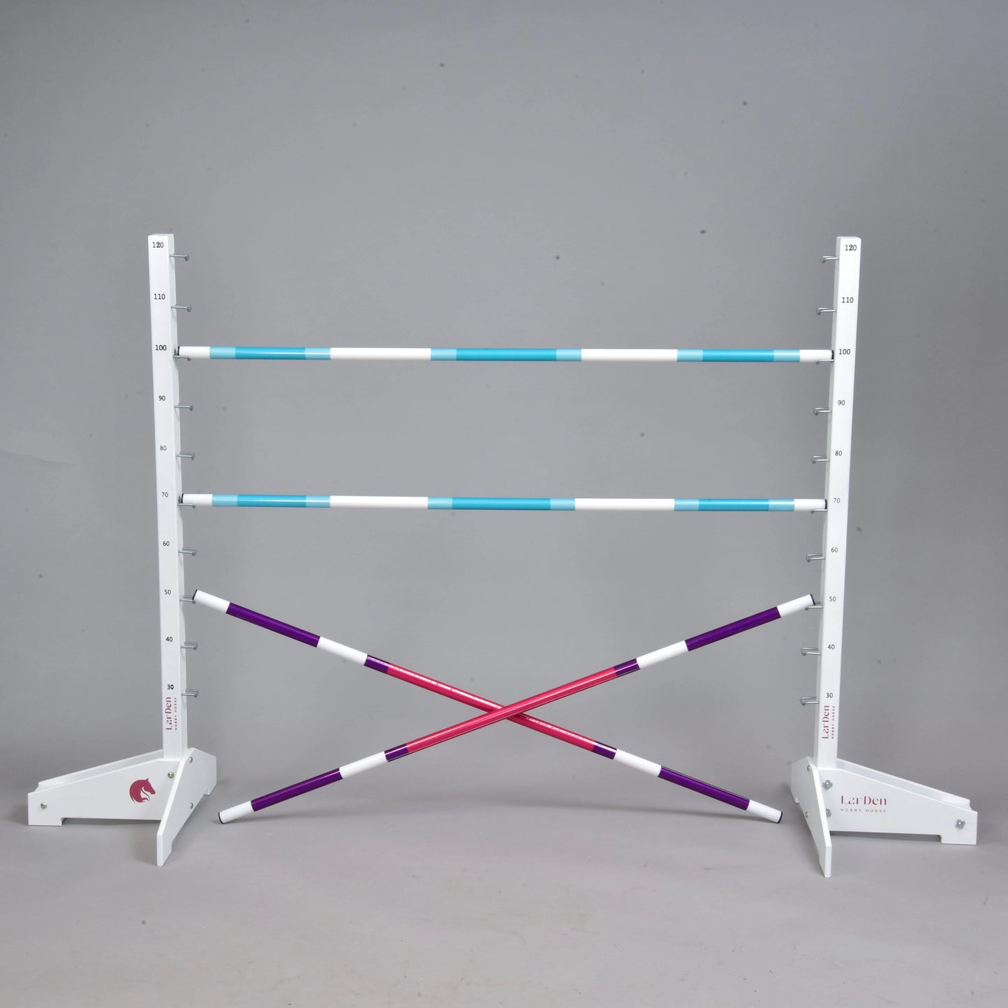 Set překážky kolmák 120 cm + 2 ks bariérky od Hobby Horse LarDen obsahuje dva bílé stojany, tři modrobílé nastavitelné tyče, dvě křížem položené fialovobílé tyče a je ideální pro Hobby Horsing uvnitř i venku. Zobrazeno na jednolitém šedém pozadí.