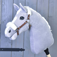 Plyšový šedý Hobby Horse od Hobby Horse LarDen s bílou hřívou a hnědou ohlávkou z koženky s beránkem, nasazený na dřevěné tyči na pozadí šedé dřevěné stěny.