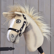 Osoba drží Hobby Horse LarDen „Hobby Horse Ivory Dream s černou ohlávkou – velikost XS“ se světle béžovou srstí, bílými znaky na hlavě, huňatou hřívou a černou ohlávkou na dřevěném pozadí.