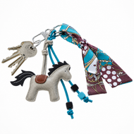 Svazek klíčů na kroužku s Přívěšek na klíče Horse Grey od Hobby Horse LarDen, modrými šňůrkami s korálky a barevným šátkem s modrým, hnědým a bílým vzorem uvázaným na kroužku na klíče.