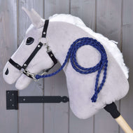 Hobby Horse - pletené vodítko Royal Blue od Hobby Horse LarDen na šedém plyšovém Hobby Horse s bílou hřívou, černou uzdečkou a královsky modrým ručně pleteným vodítkem, připevněném na dřevěné stěně s tyčí zajištěnou černým kovovým držákem.