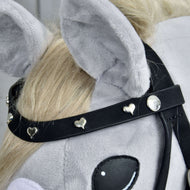 Detail hlavy šedého plyšového Hobby Horse s kompletní uzdečkou De Luxe se 2 čelenkami od Hobby Horse LarDen, se dvěma odnímatelnými čelenkami zdobenými malými stříbrnými srdíčky a kulatými cvočky. Kůň má světle blond hřívu a velké měkké uši.