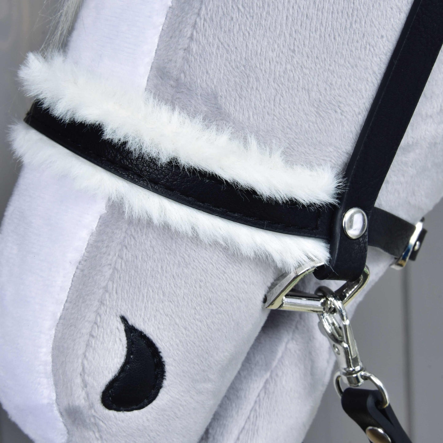 Detail Kompletní uzdečky s beránkem černé od Hobby Horse LarDen: měkká světle šedá plyšová koňská hlava s koženkovou uzdečkou, bílým lemováním z umělé kožešiny, černým půlměsícovým detailem nozdr y a jemně strukturovaným povrchem.