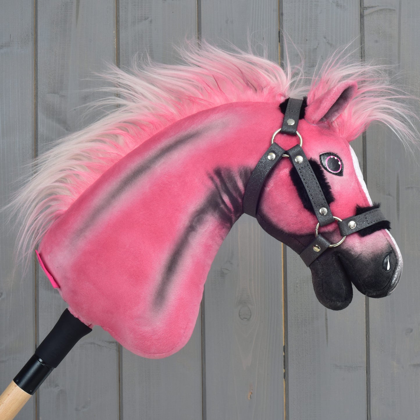Limitovaná edice Hobby Horse LarDen Pinkie s třpytivou ohlávkou a dřevěnou tyčí, umístěná před pozadím ze šedých dřevěných panelů.