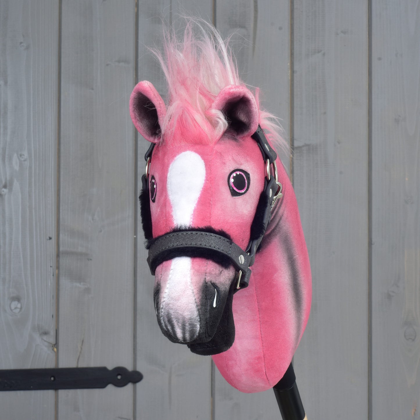 Limitovaná edice Hobby Horse LarDen Pinkie s třpytivou ohlávkou, s růžovobílým plyšem a huňatou růžovou hřívou, umístěná před šedým dřevěným pozadím.