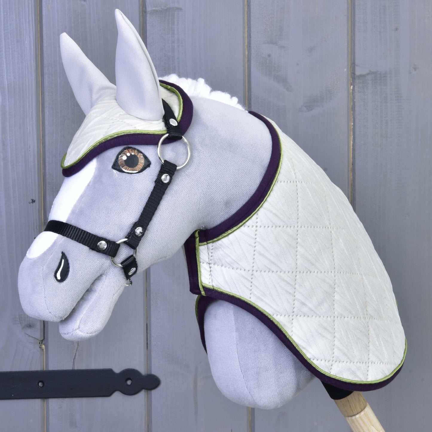Set Leonardo od Hobby Horse LarDen se šedým plyšovým Hobby Horse s bílou prošívanou dekou, ladící čabrakou, černou uzdečkou a otěžemi na dřevěné tyči, zobrazený na pozadí šedé dřevěné stěny.