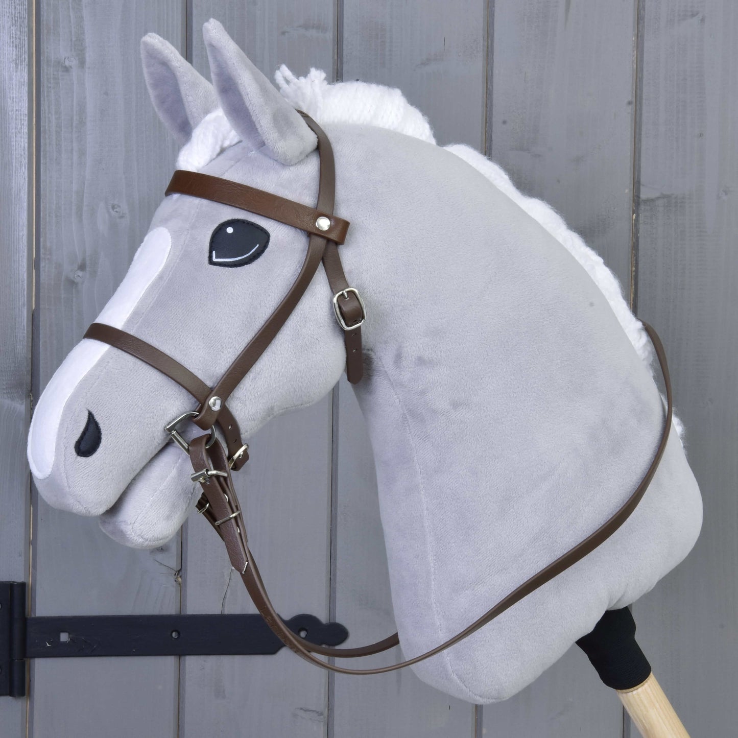 Hobby Horse LarDen, šedá hračka koně na tyči s bílou hřívou, přívětivým výrazem a Kompletní uzdečka s nánosníkem Brown, na šedém dřevěném pozadí.
