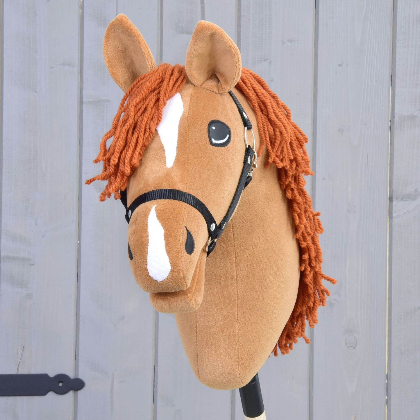 Hobby Horse Little Angel s černou ohlávkou od Hobby Horse LarDen má vzhled ryzáka českého teplokrevníka, bílou lysinu a bílé znaky na nose, oranžovou hřívu z příze a je zobrazen na světle šedém dřevěném pozadí.