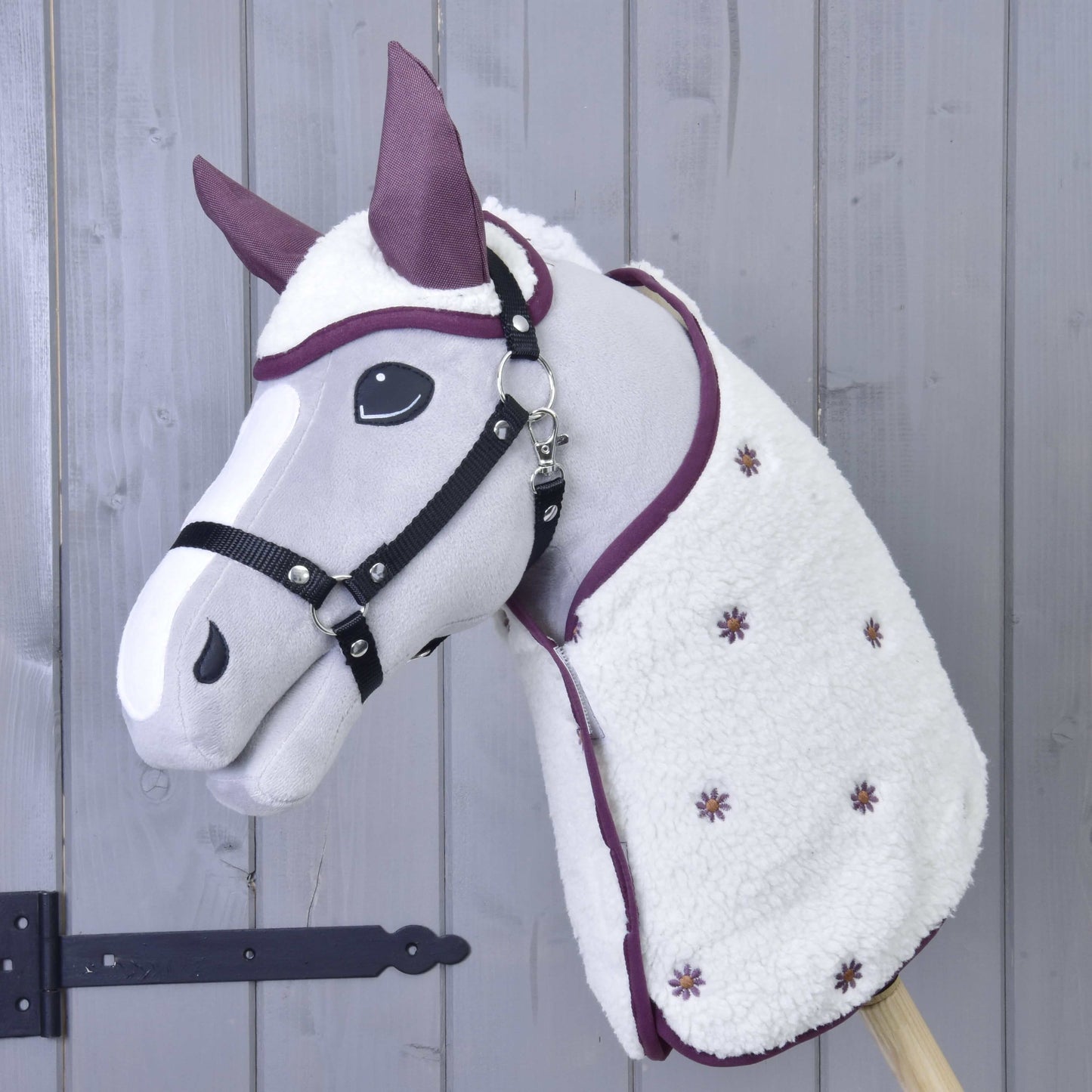 Set Loret od Hobby Horse LarDen má plyšového Hobby Horse se šedým obličejem, černou uzdečkou, fialovými detaily, čabrakou a bílou dekou s drobnými fialovými květy, naaranžovaného před stěnou z dřevěných panelů.