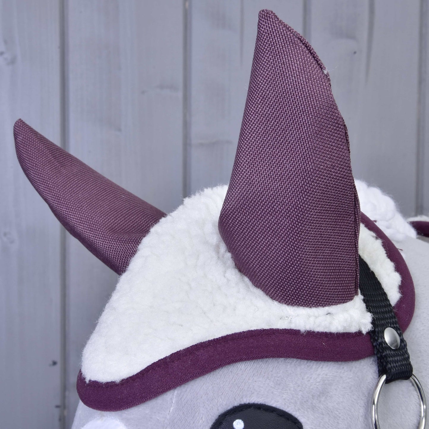 Detail plyšové zvířecí hlavy Set Loret od Hobby Horse LarDen s bílou chlupatou látkou, velkými fialovými ušima ve stylu čabraky a černým páskem na světle šedém dřevěném pozadí.